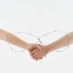 Two hands clasped within a circular barbed wire loop, symbolizing complex relationships.