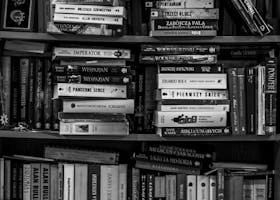 A black and white image of a packed bookshelf with various books in a library setting.