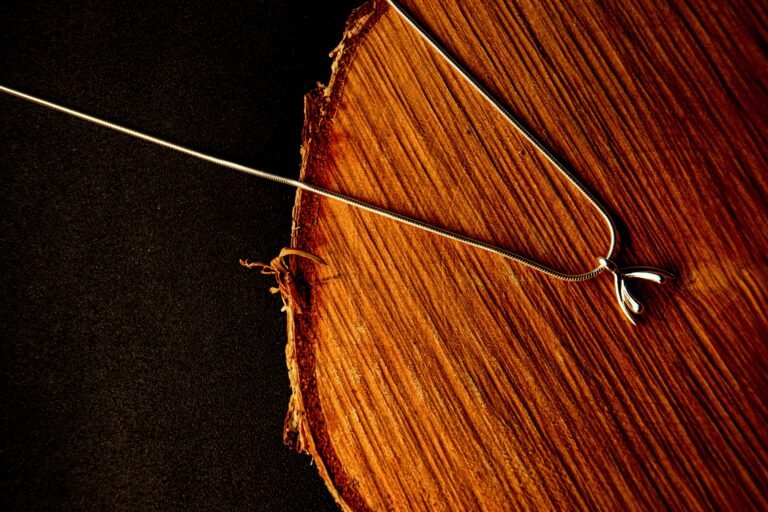 Close-up of a silver necklace with a wishbone pendant on a natural wooden surface, elegant and stylish.