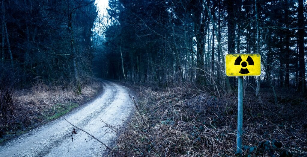 A radiation warning sign by a forest pathway in a gloomy setting.