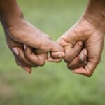 A touching moment as a couple holds hands with a green backdrop, symbolizing unity and connection.